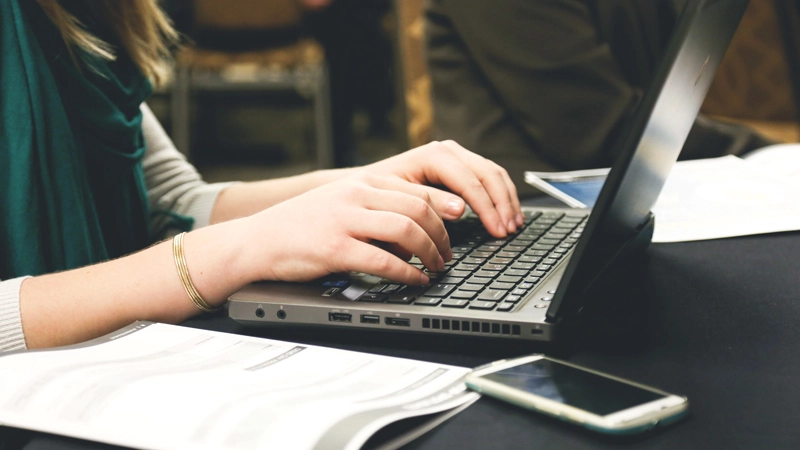 Person typing on a laptop with documents and a phone nearby